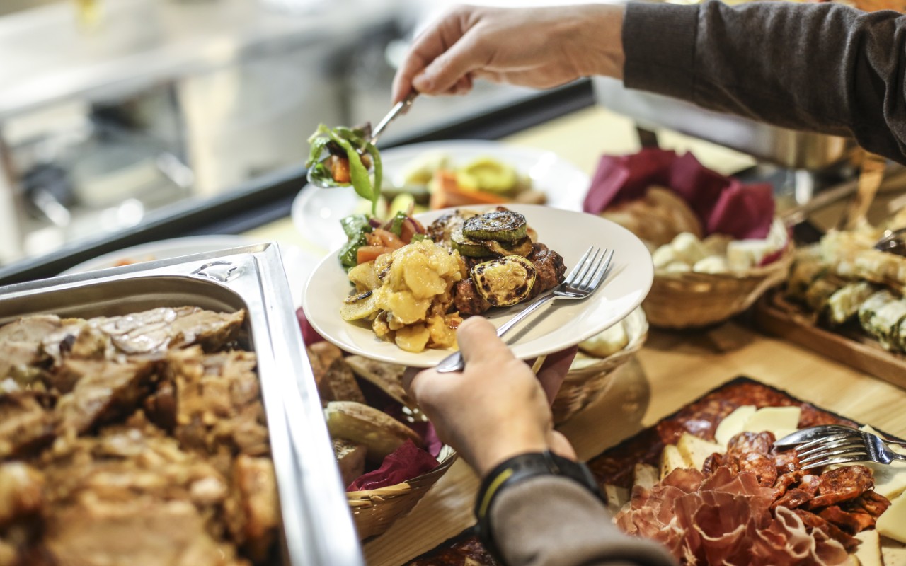 Person serving food from buffet table.